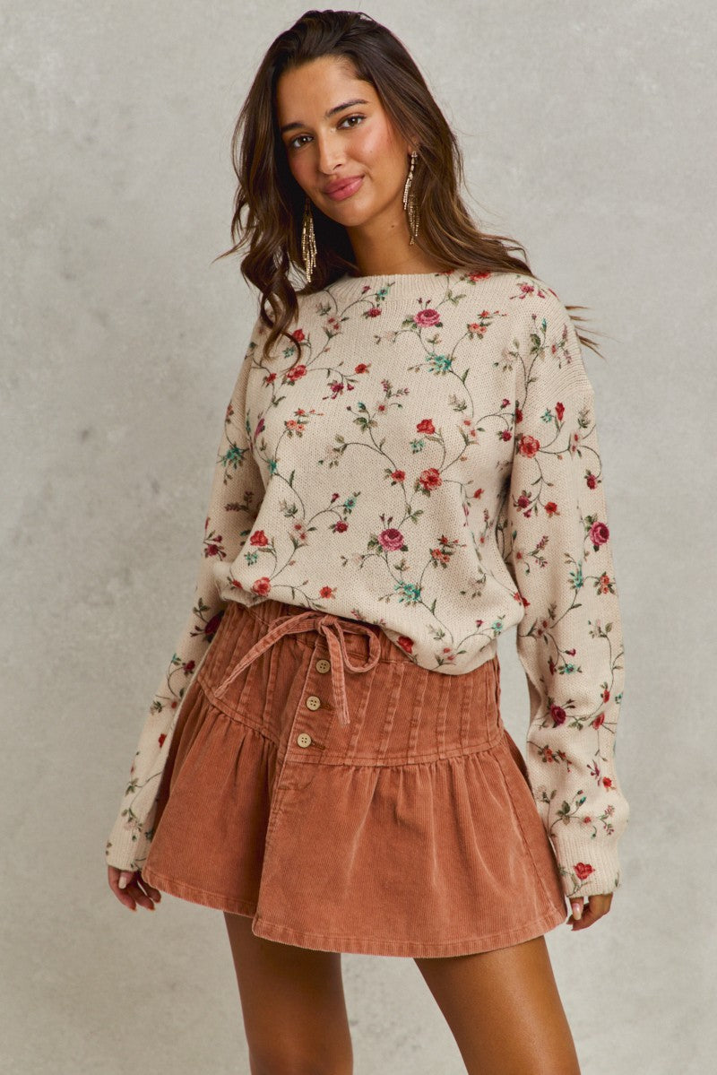 Woman wearing a floral sweater and brown skirt against a plain background