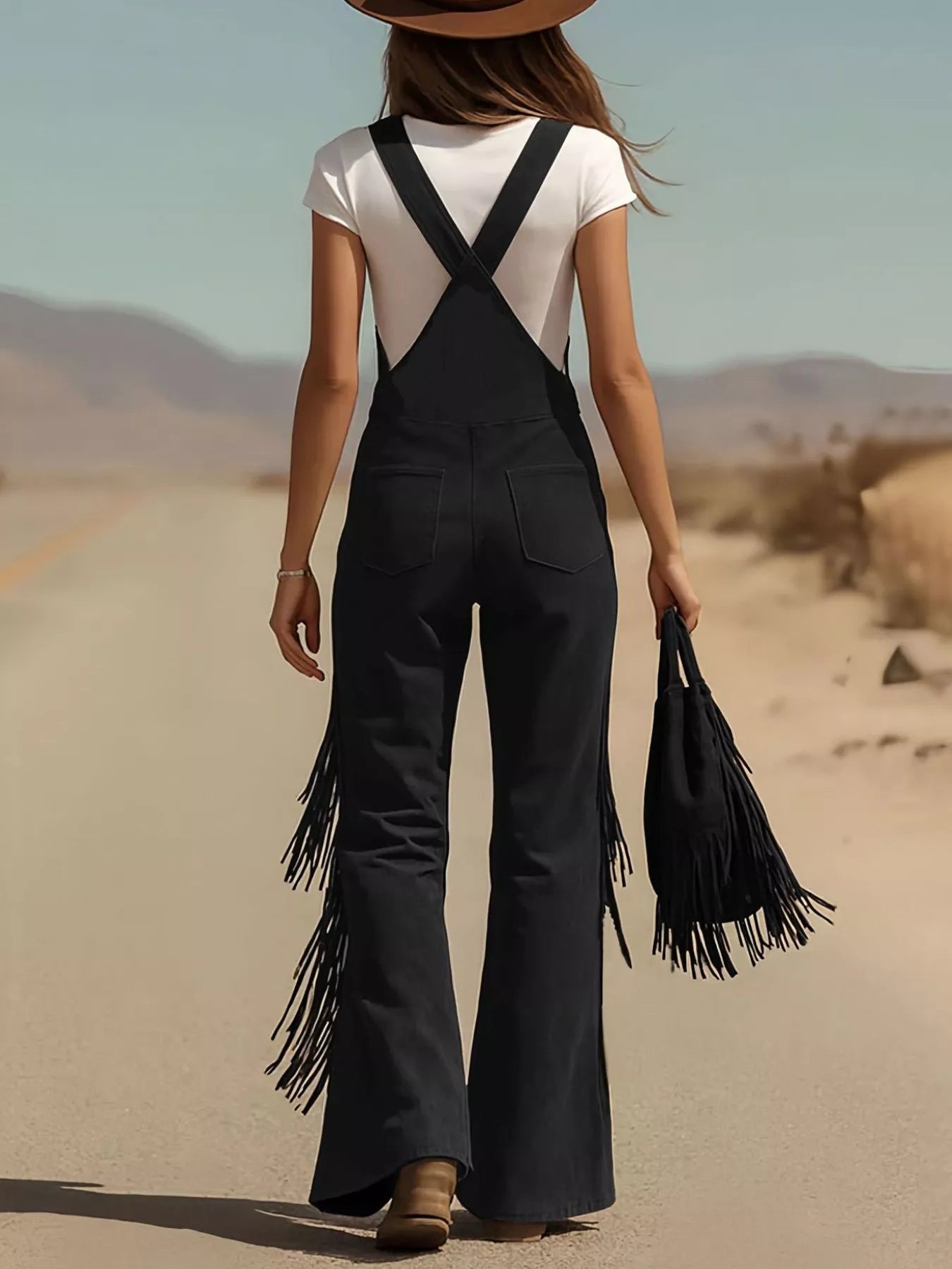 Person wearing black fringed overalls and a white top in a desert setting