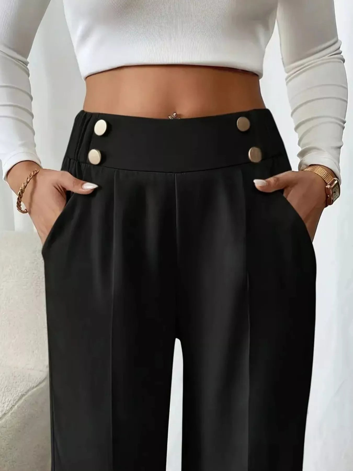 Black high-waisted pants with button details worn by a person, on a neutral background