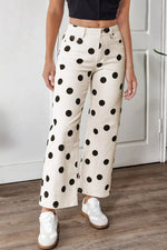 Person wearing white pants with black polka dots and white sneakers indoors.
