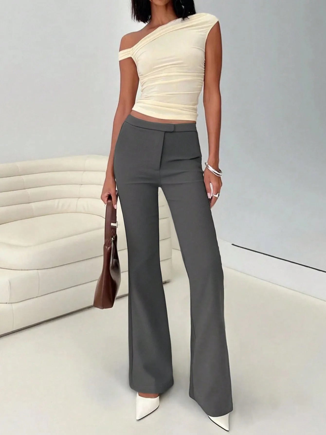 Woman wearing a beige one-shoulder top and gray high-waisted pants in an indoor setting.
