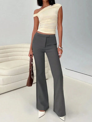 Woman wearing a beige one-shoulder top and gray high-waisted pants in an indoor setting.