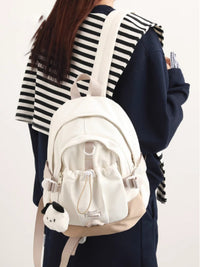 Person wearing a white backpack with a small plush toy attached, on a plain background