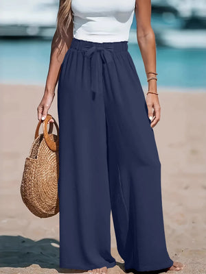 Person wearing navy wide-leg pants and a white top on a beach.