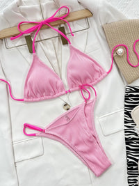 Pink bikini set on a white surface with accessories.