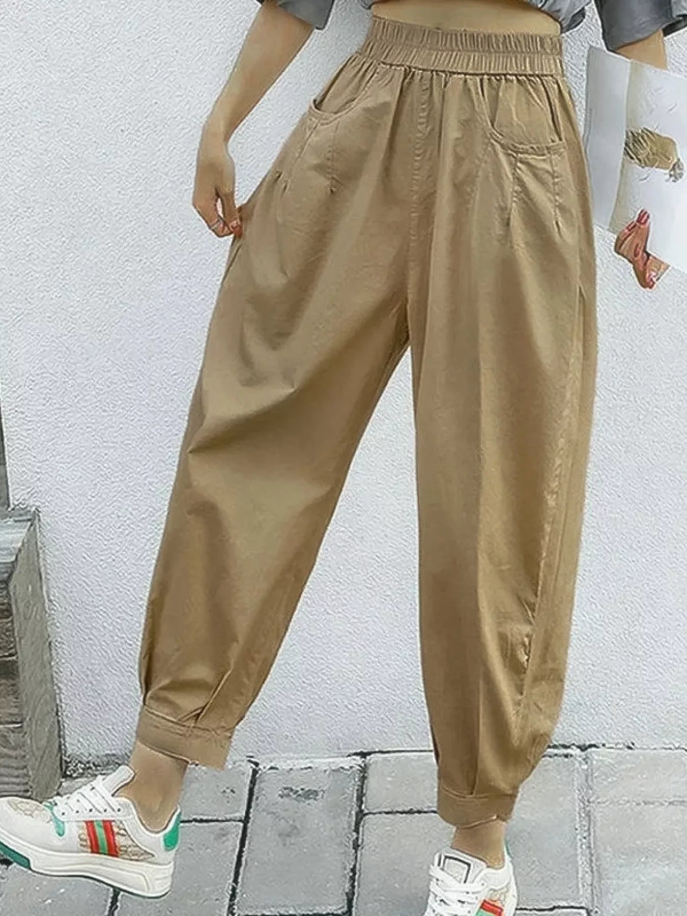 Person wearing beige jogger pants and white sneakers against a light gray wall.