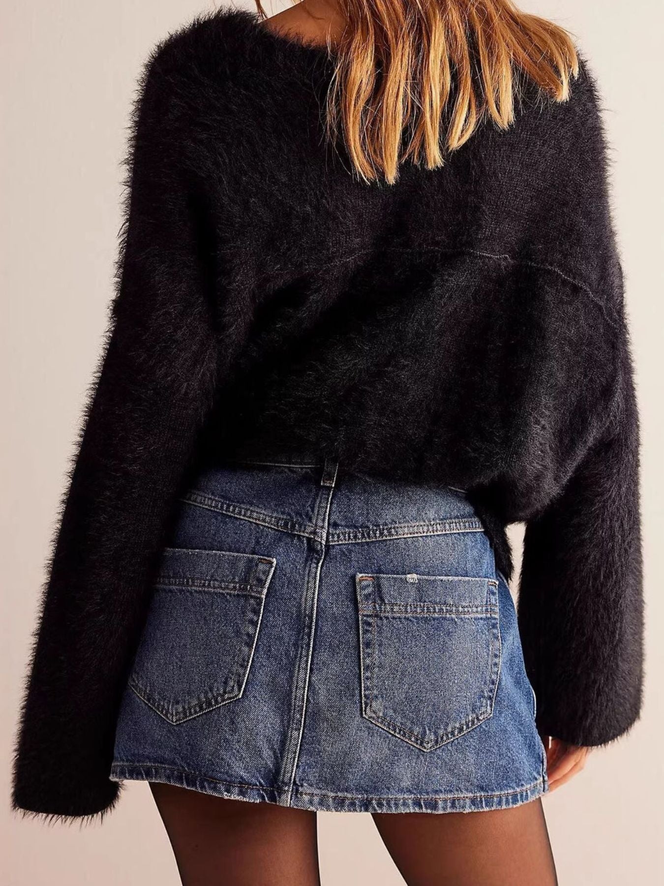 Person wearing a black fuzzy sweater and denim skirt on a plain background