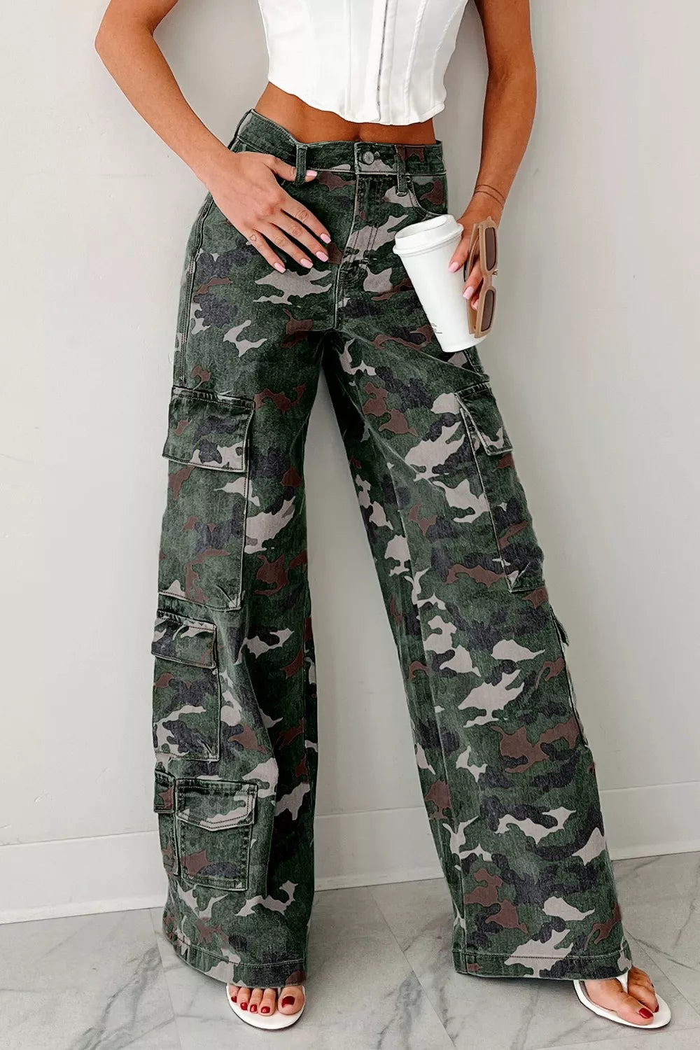 Person wearing camouflage cargo pants with a white top and sandals on a light background