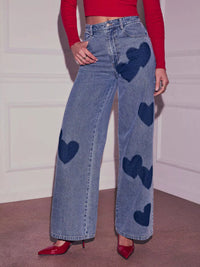 Person wearing blue jeans with heart patterns and a red top indoors.