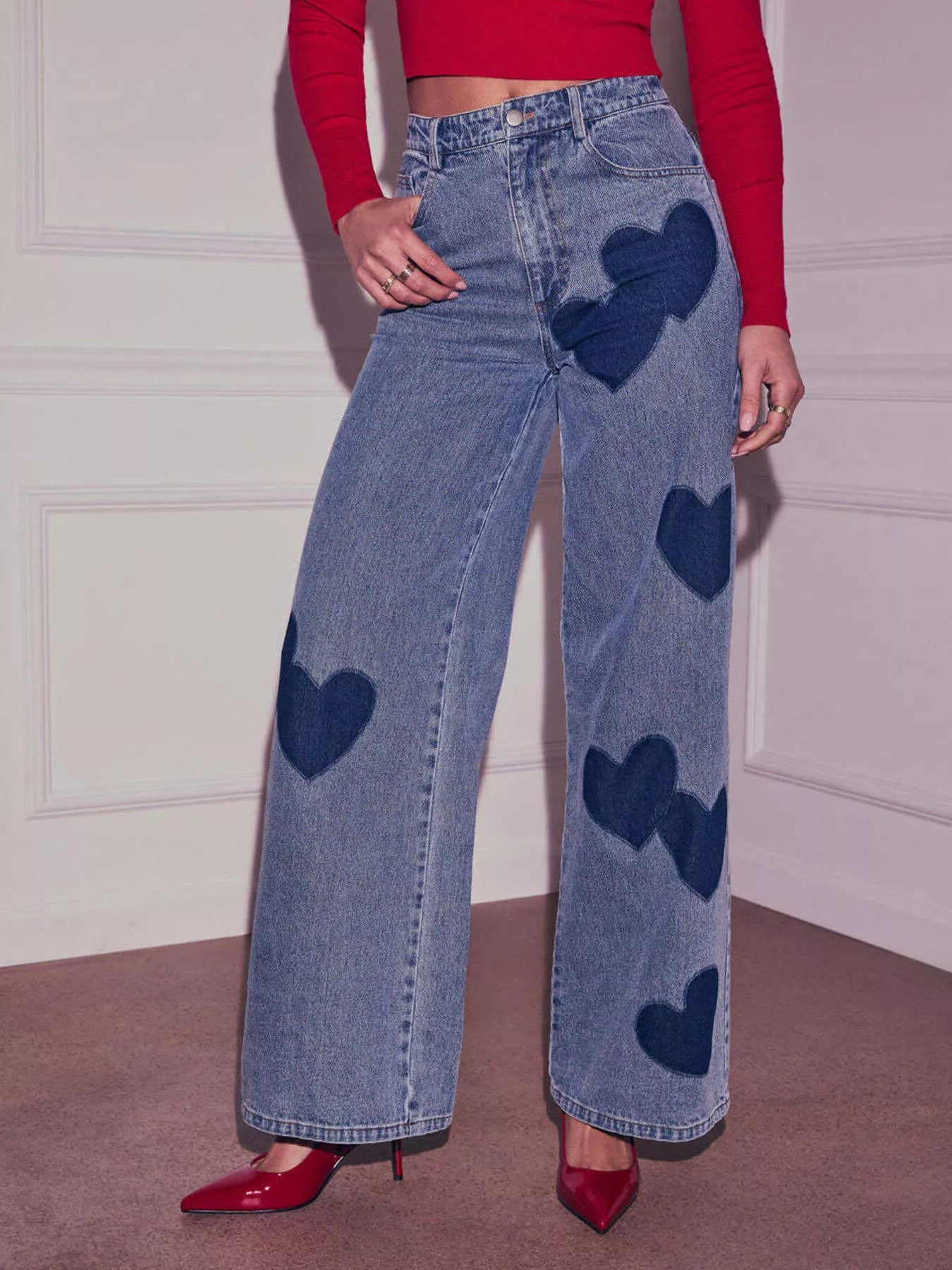Person wearing blue jeans with heart patterns and a red top indoors.
