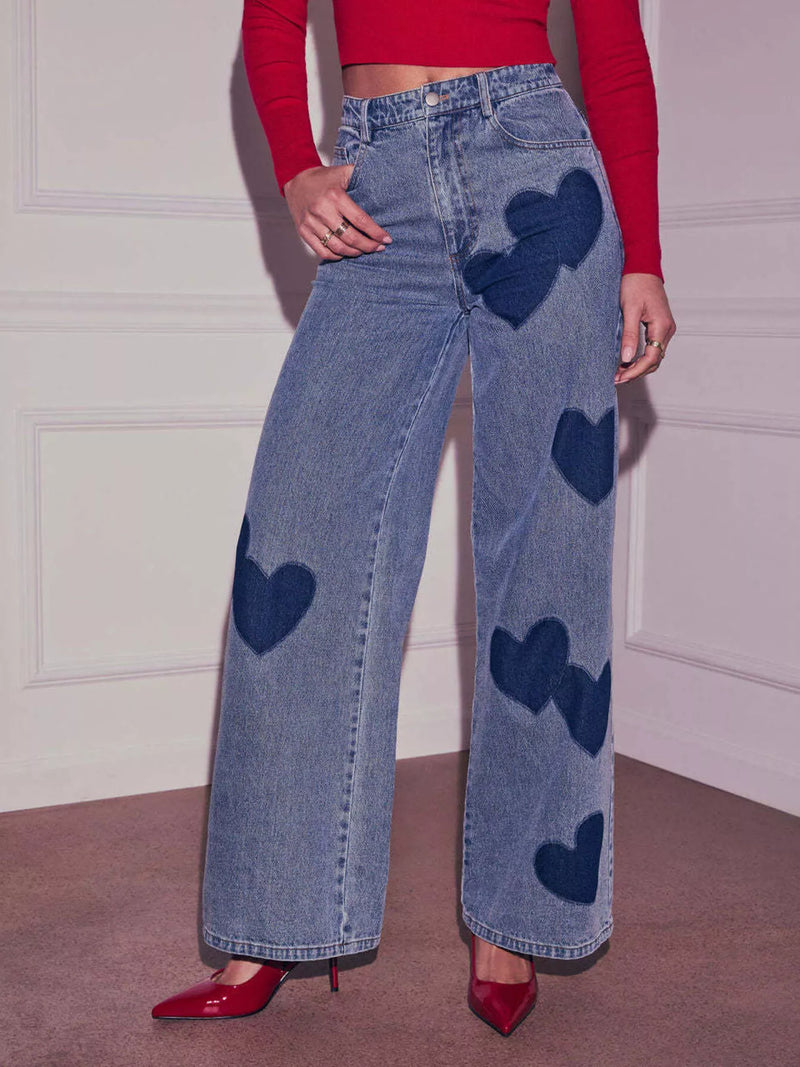 Person wearing blue jeans with heart patterns and a red top indoors.