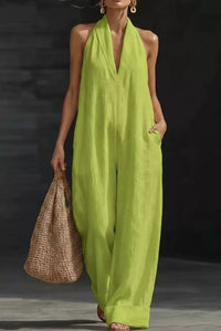 Woman wearing a bright green jumpsuit holding a woven bag against a dark background
