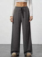 Person wearing gray wide-leg pants with a white top on a plain background