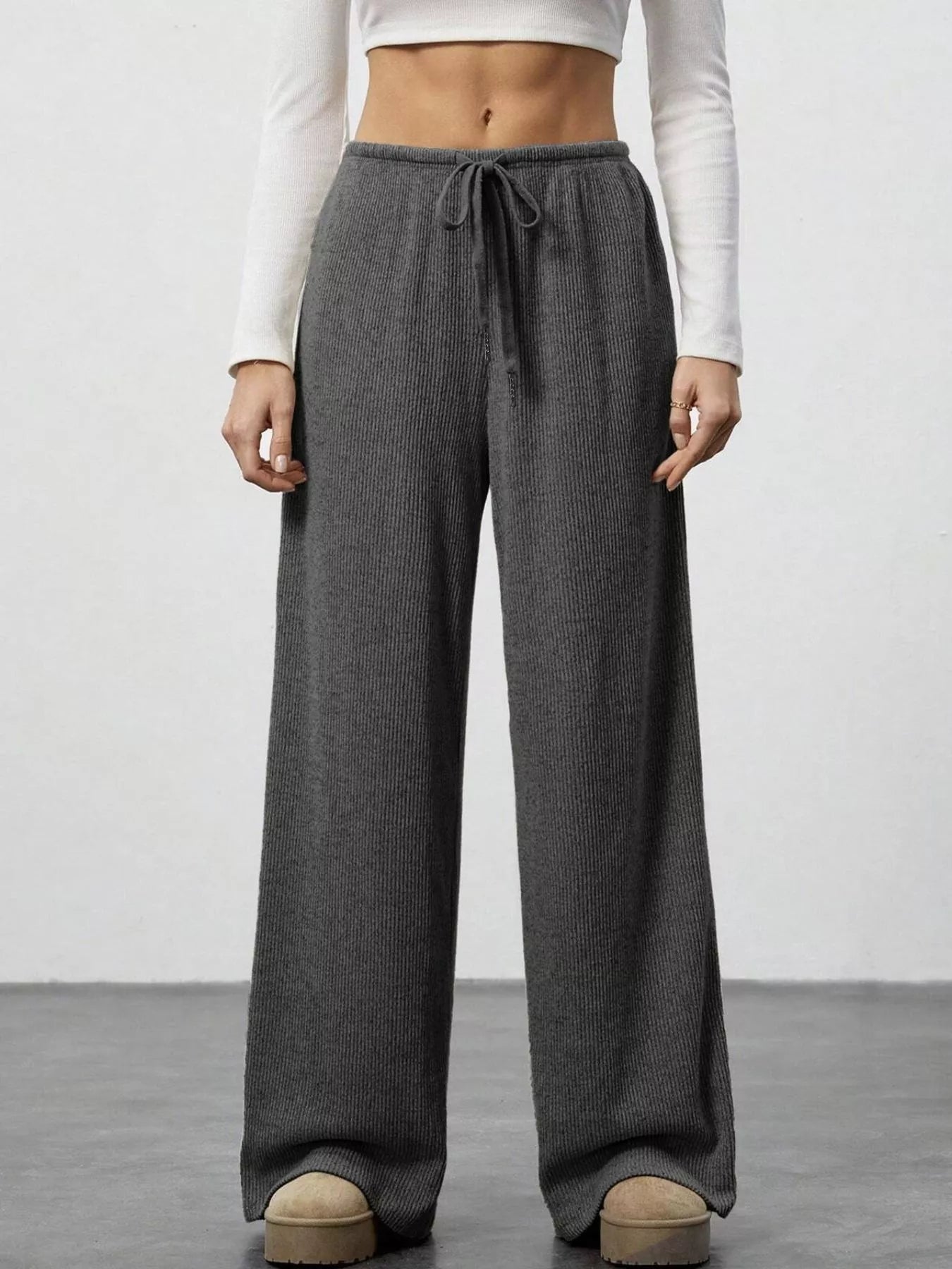 Person wearing gray wide-leg pants with a white top on a plain background