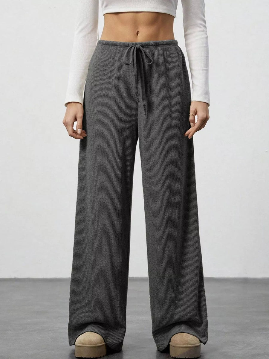 Person wearing gray wide-leg pants with a white top on a plain background