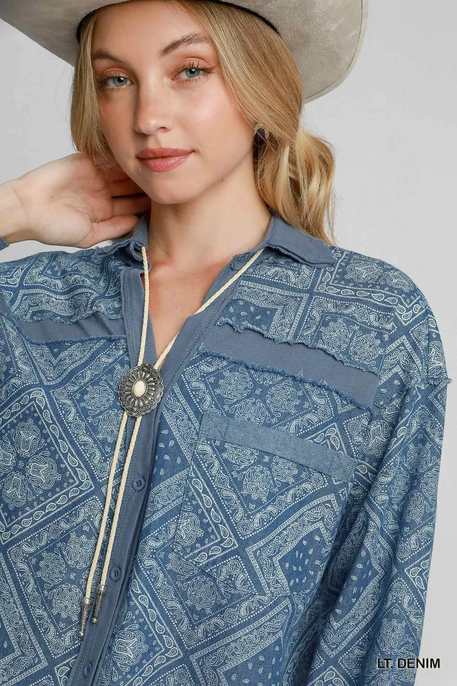 Woman wearing a blue patterned shirt with a beige hat on a plain background