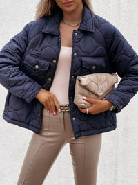 Person wearing a navy quilted jacket holding a beige clutch against a light background