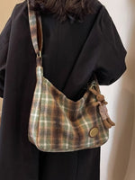 Plaid shoulder bag with drawstring and decorative element worn by a person against a neutral background
