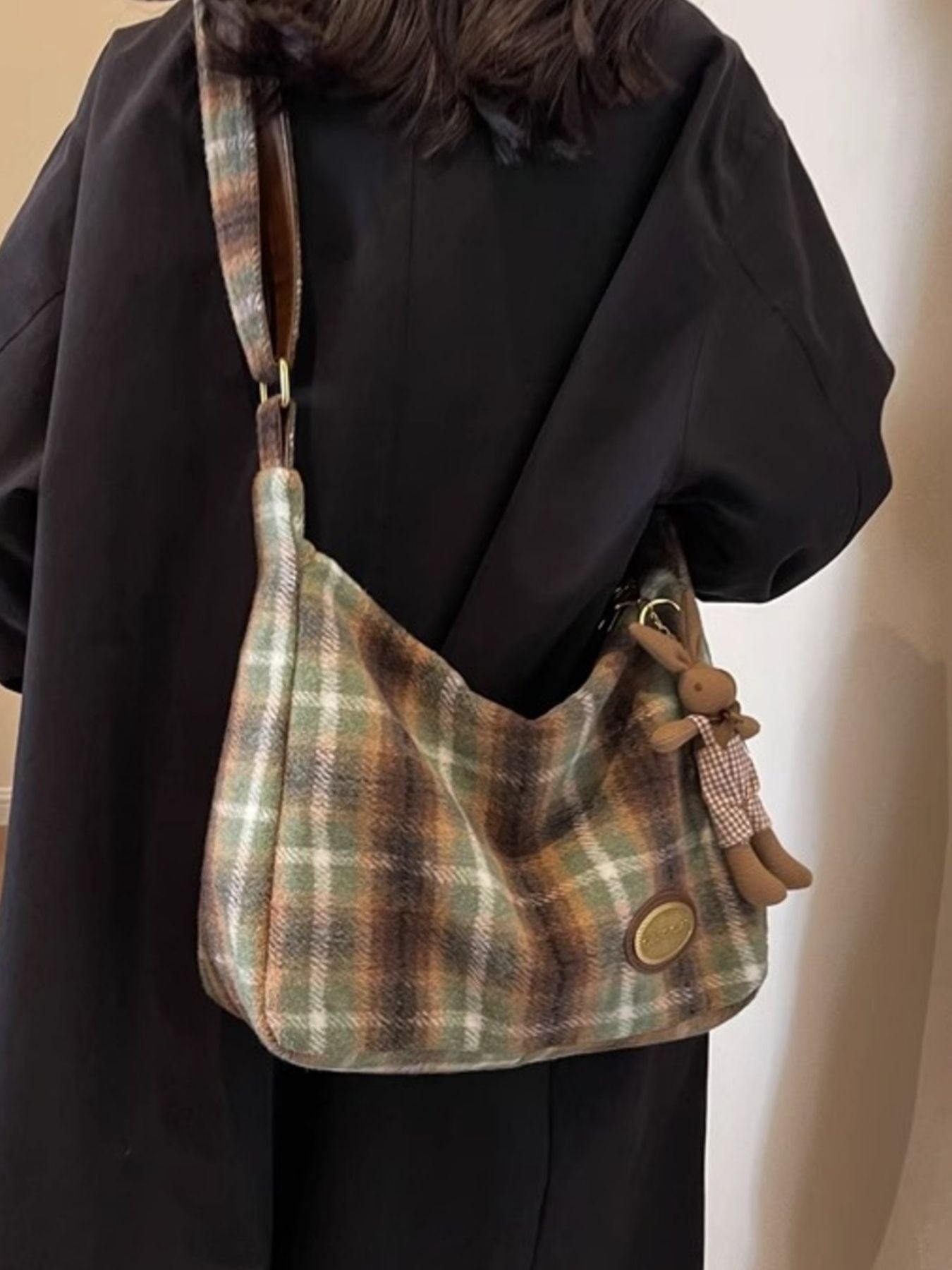 Plaid shoulder bag with drawstring and decorative element worn by a person against a neutral background