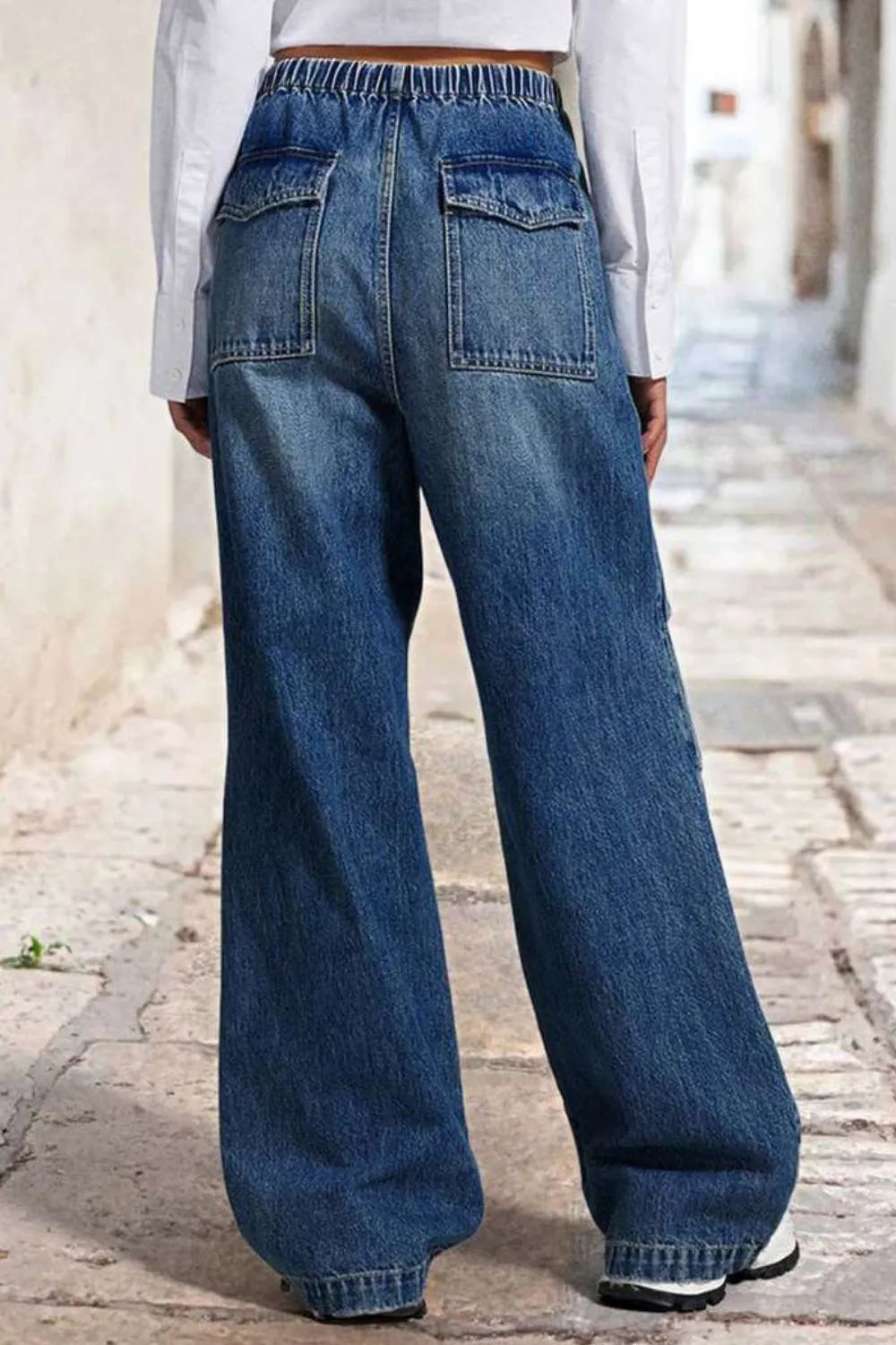 Person wearing blue wide-leg jeans on a stone pavement.