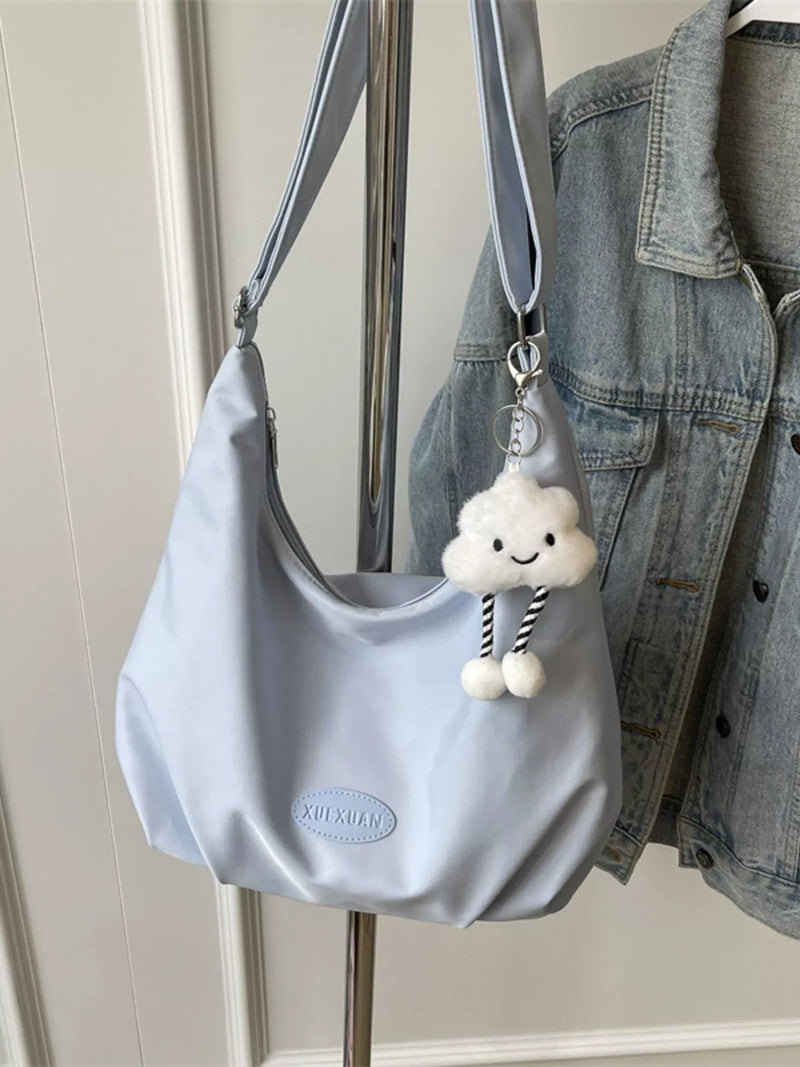 Light blue handbag with a cloud-shaped charm hanging on a hook, next to a denim jacket.