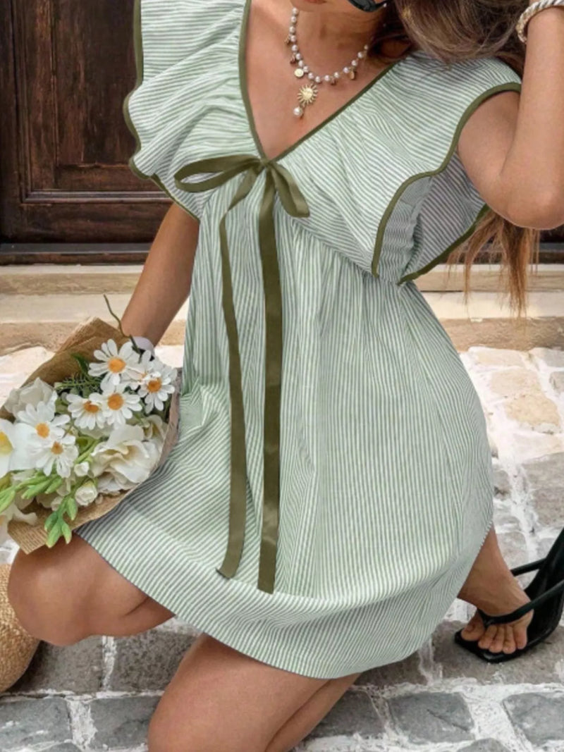 Woman wearing a green and white striped dress with a bow, holding flowers on a stone path.