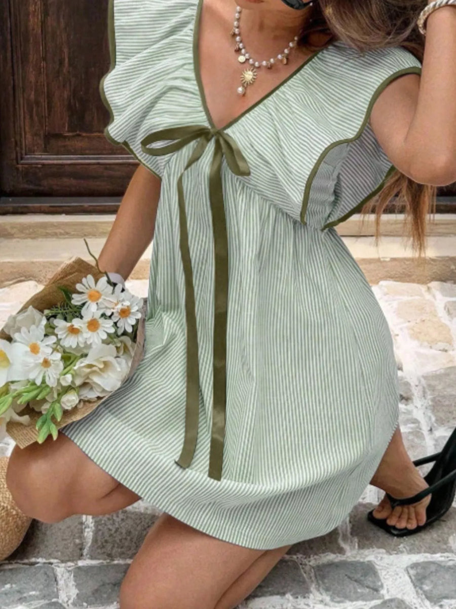 Woman wearing a green and white striped dress with a bow, holding flowers on a stone path.