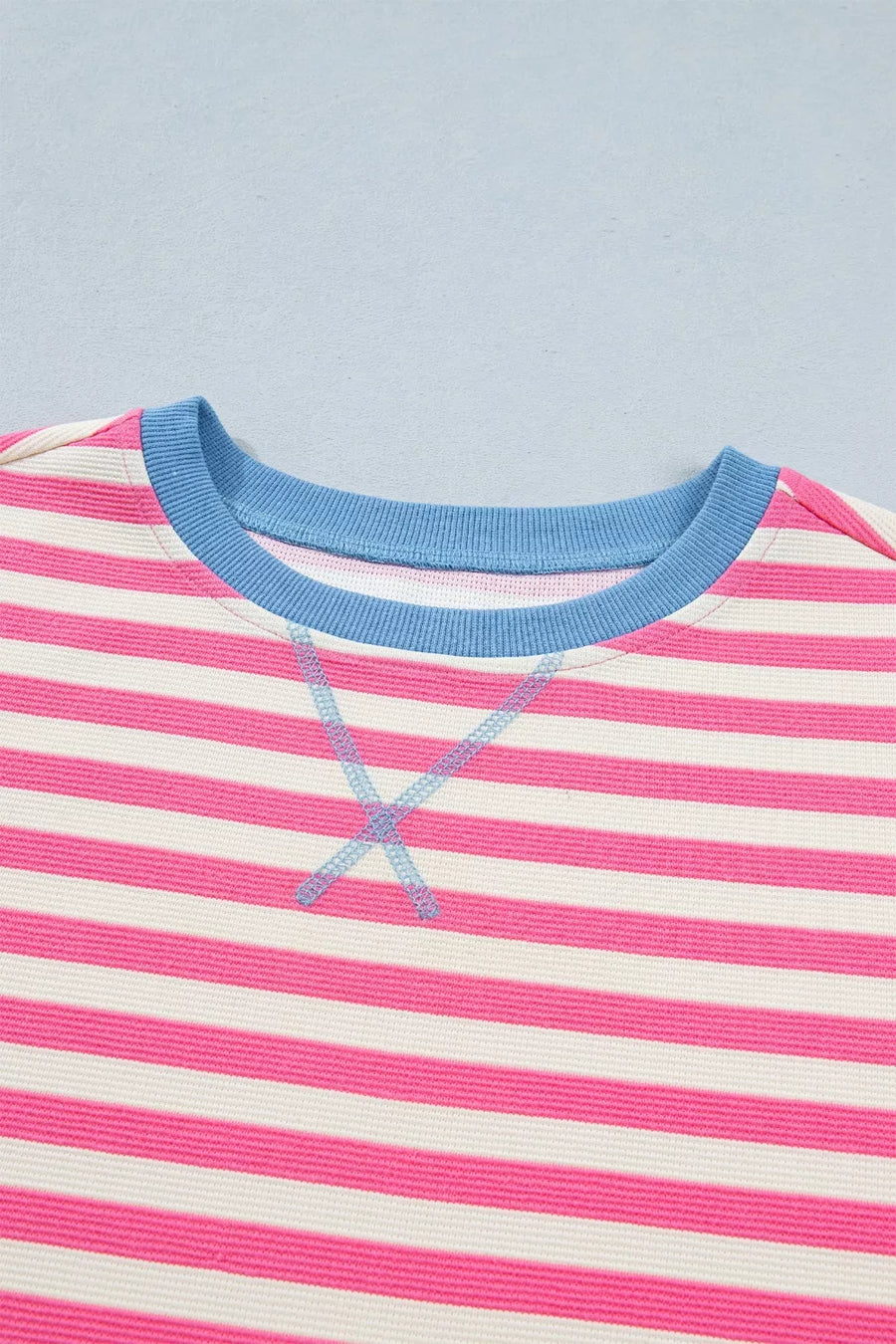 Close-up of a pink and white striped shirt with blue trim on a light blue background