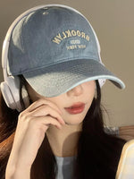 Person wearing a denim cap with 'Brooklyn' text and headphones, against a neutral background