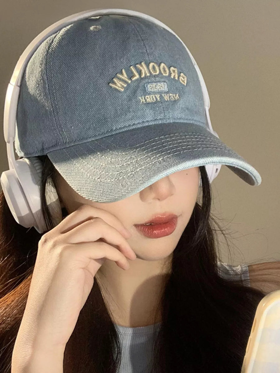 Person wearing a denim cap with 'Brooklyn' text and headphones, against a neutral background