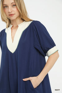Woman wearing a navy blue dress with white trim on a white background