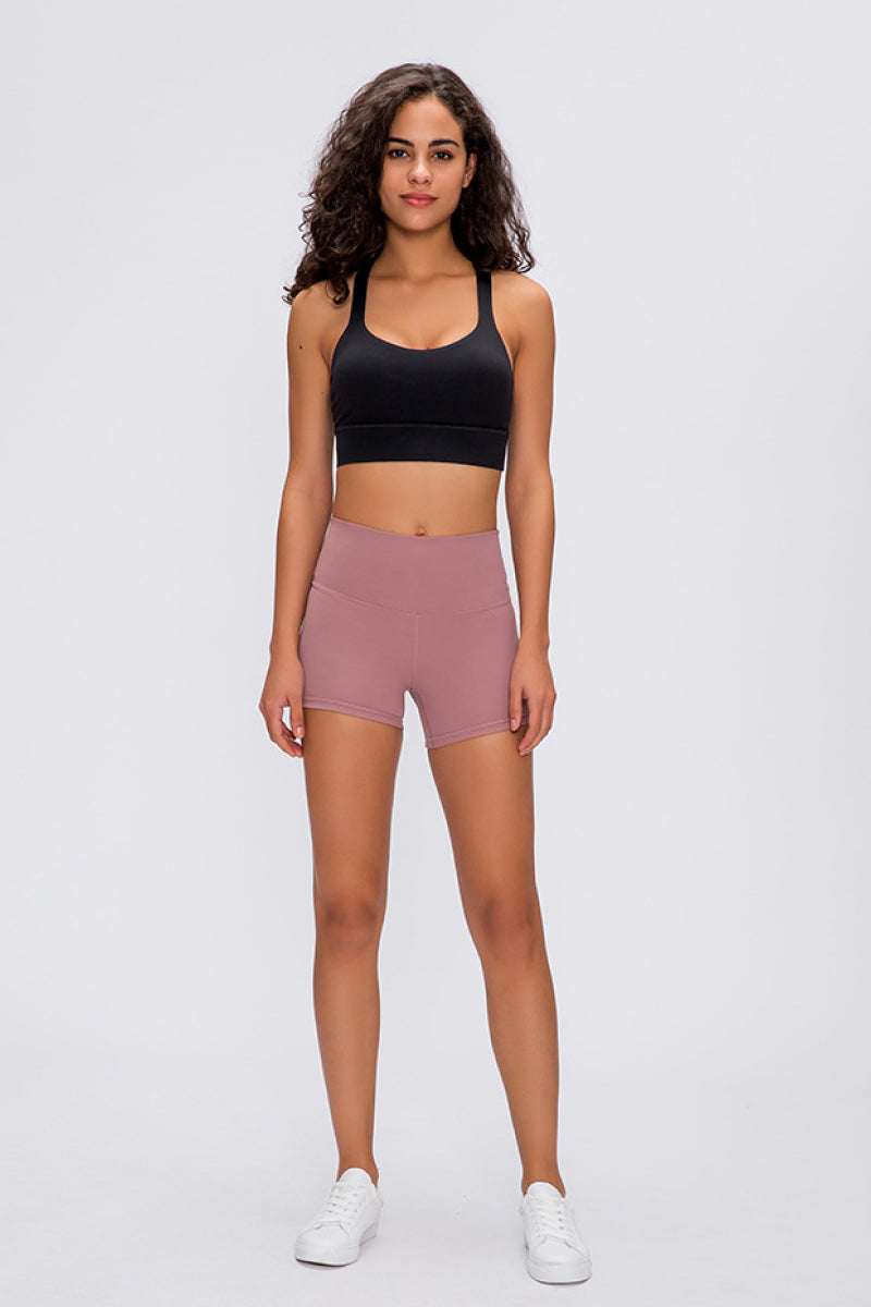 Woman wearing a black sports bra and pink shorts on a white background