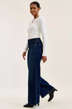 Woman wearing a white top and blue jeans on a plain background