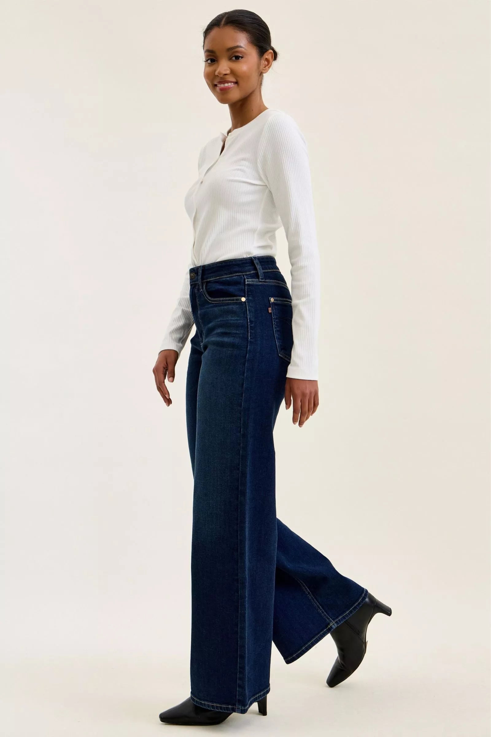 Woman wearing a white top and blue jeans on a plain background
