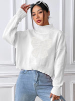 Woman wearing a white sweater and blue jeans against a white paneled wall.