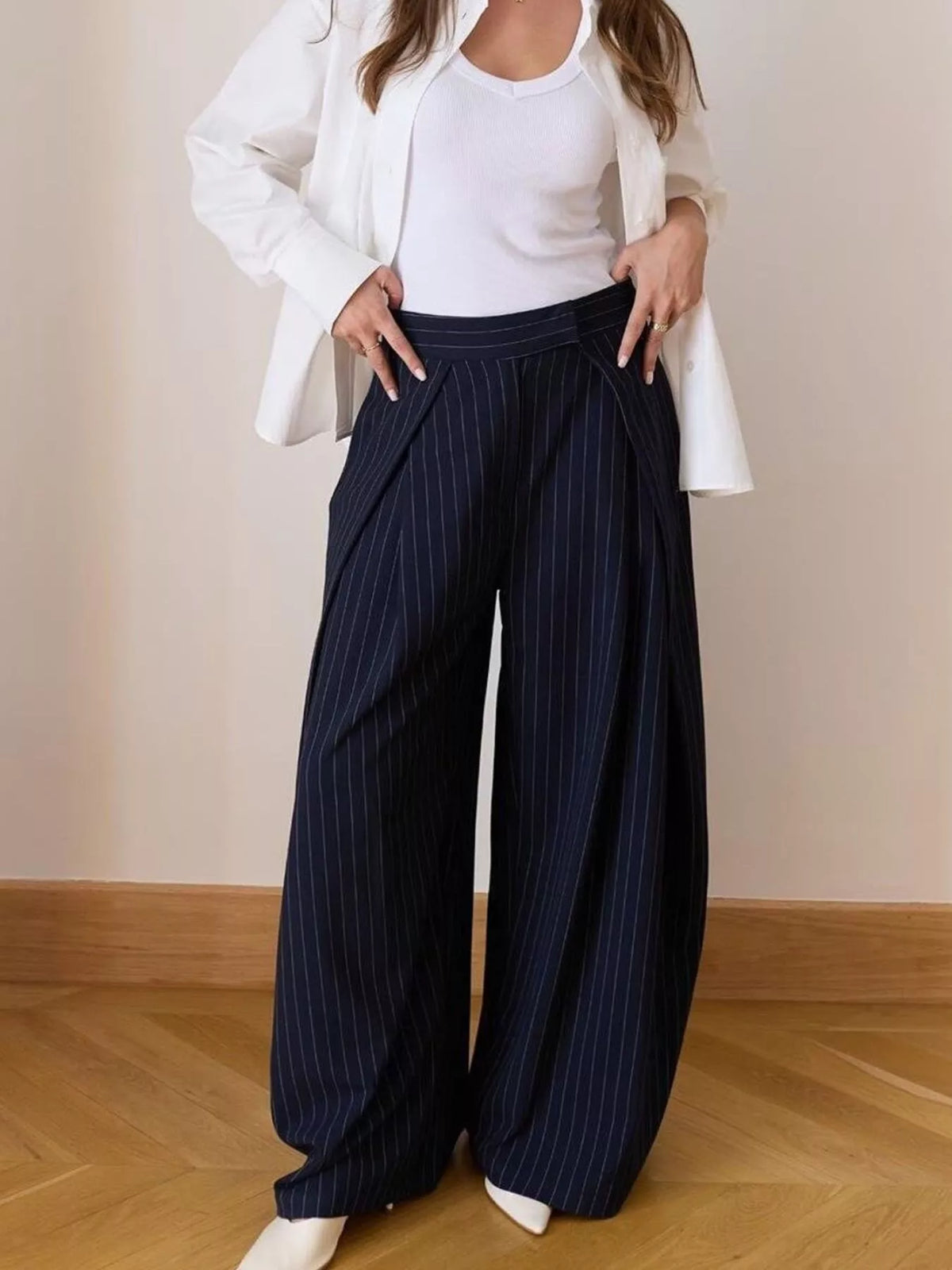 Person wearing navy pinstripe wide-leg pants with a white top and jacket on a plain background