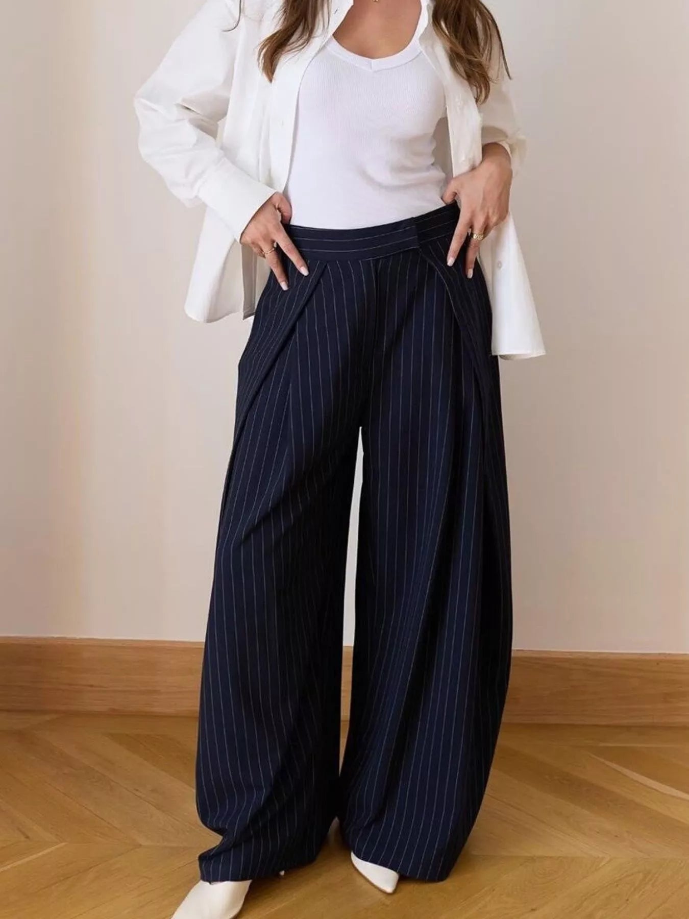 Person wearing navy pinstripe wide-leg pants with a white top and jacket on a plain background