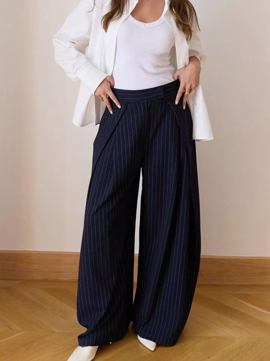 Person wearing navy pinstripe wide-leg pants with a white top and jacket on a plain background