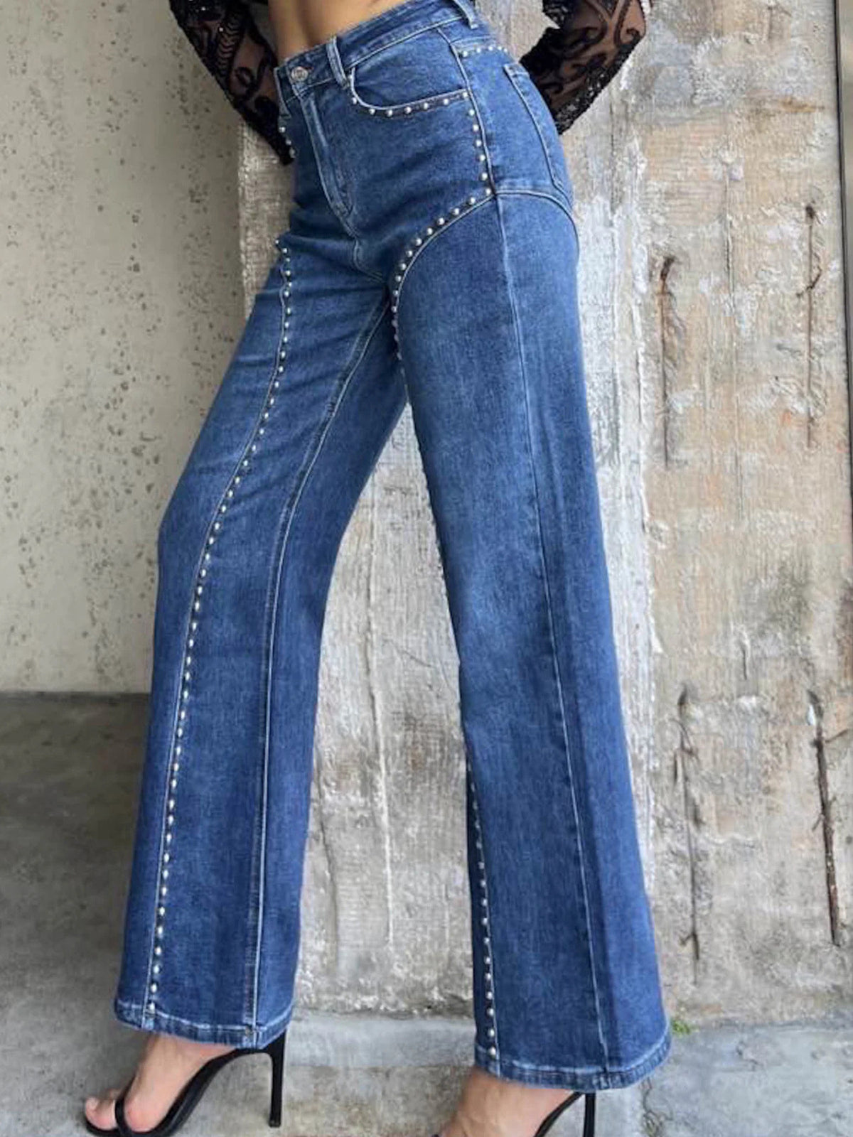 Blue jeans worn by a person against a textured wall.