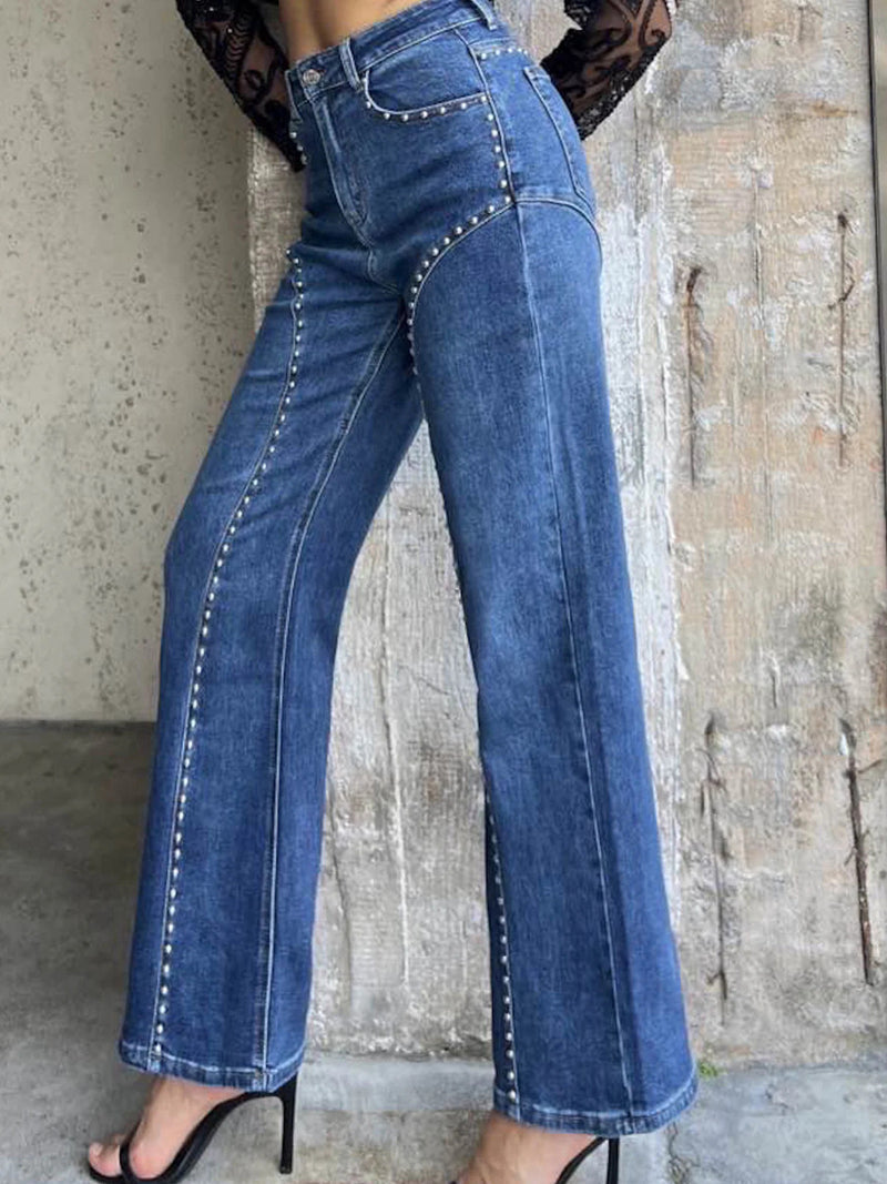 Blue jeans worn by a person against a textured wall.