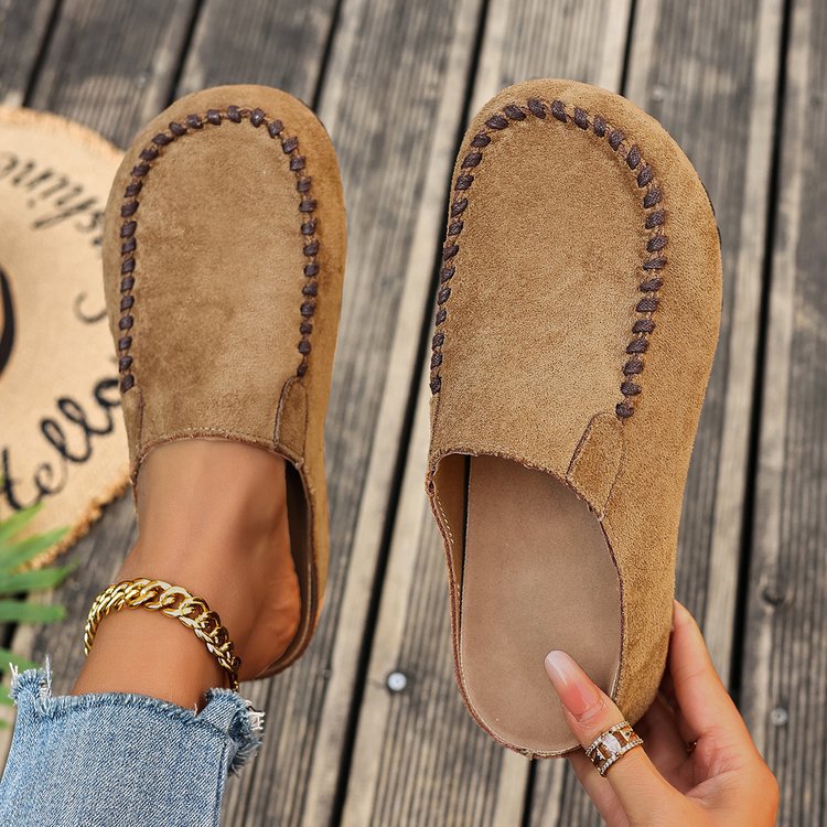 Brown suede slippers being held on a wooden floor