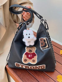 Black handbag with teddy bear and 'B Strong' patches held by a person.