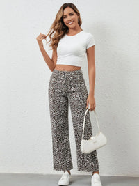 Woman wearing a white crop top and leopard print pants, holding a white handbag against a light gray background.