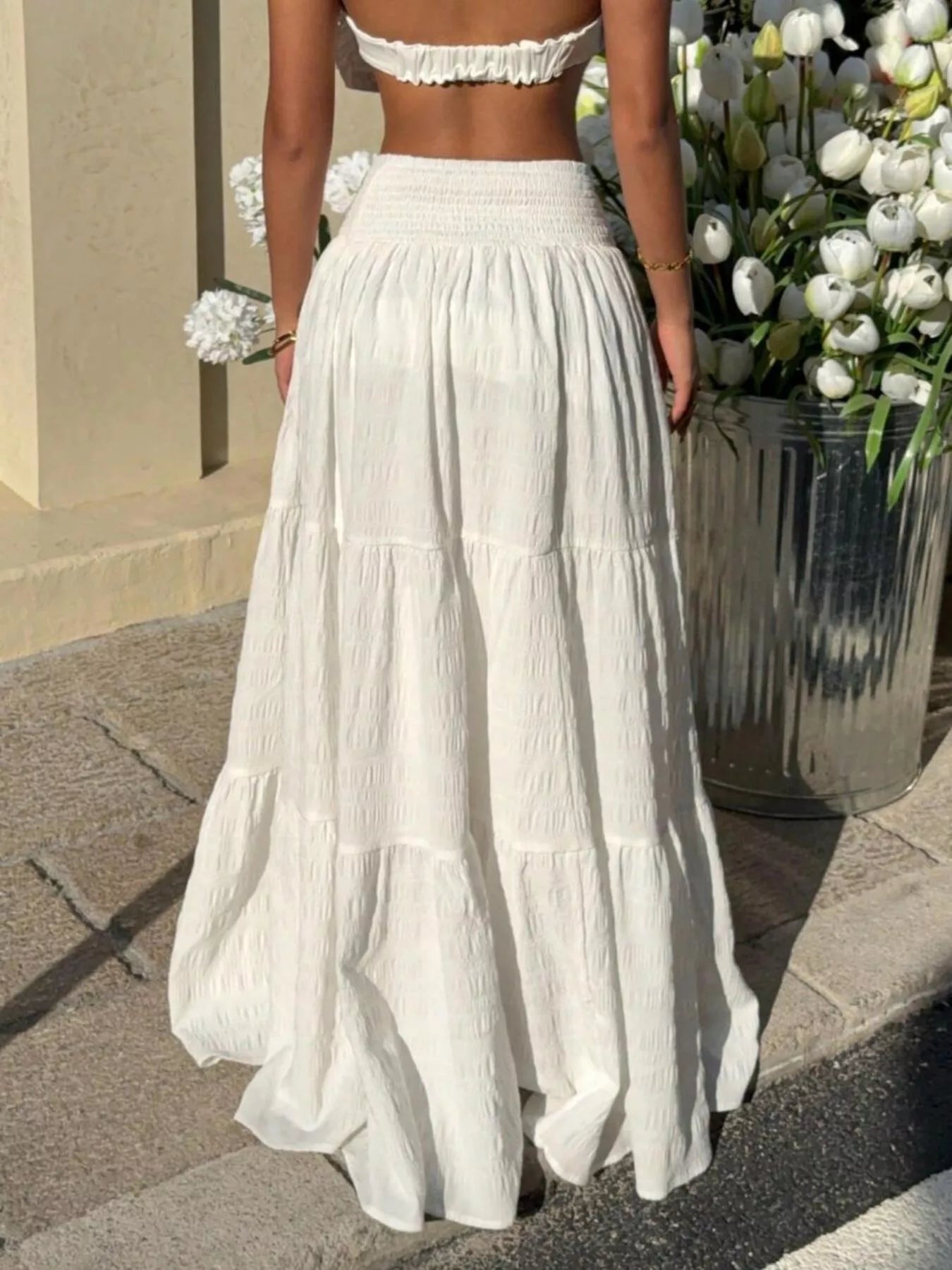 Person wearing a white dress standing next to a planter with flowers.