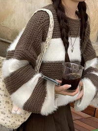 Person wearing a brown and white striped sweater holding a glass of dark liquid.