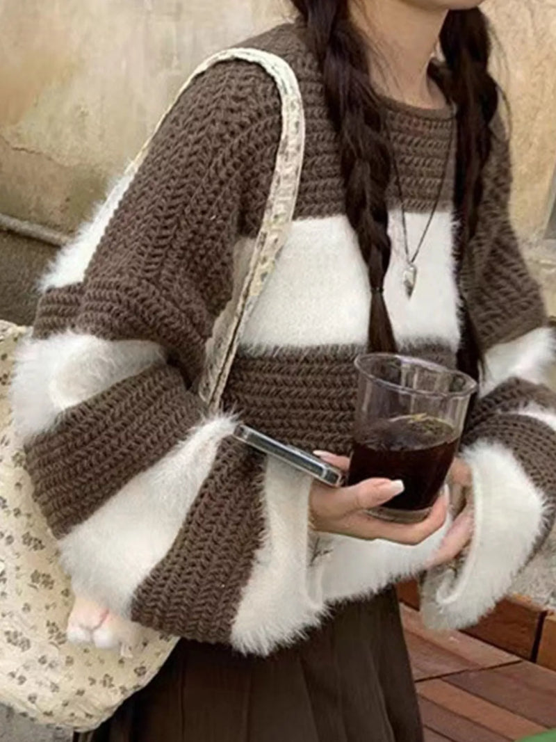 Person wearing a brown and white striped sweater holding a glass of dark liquid.
