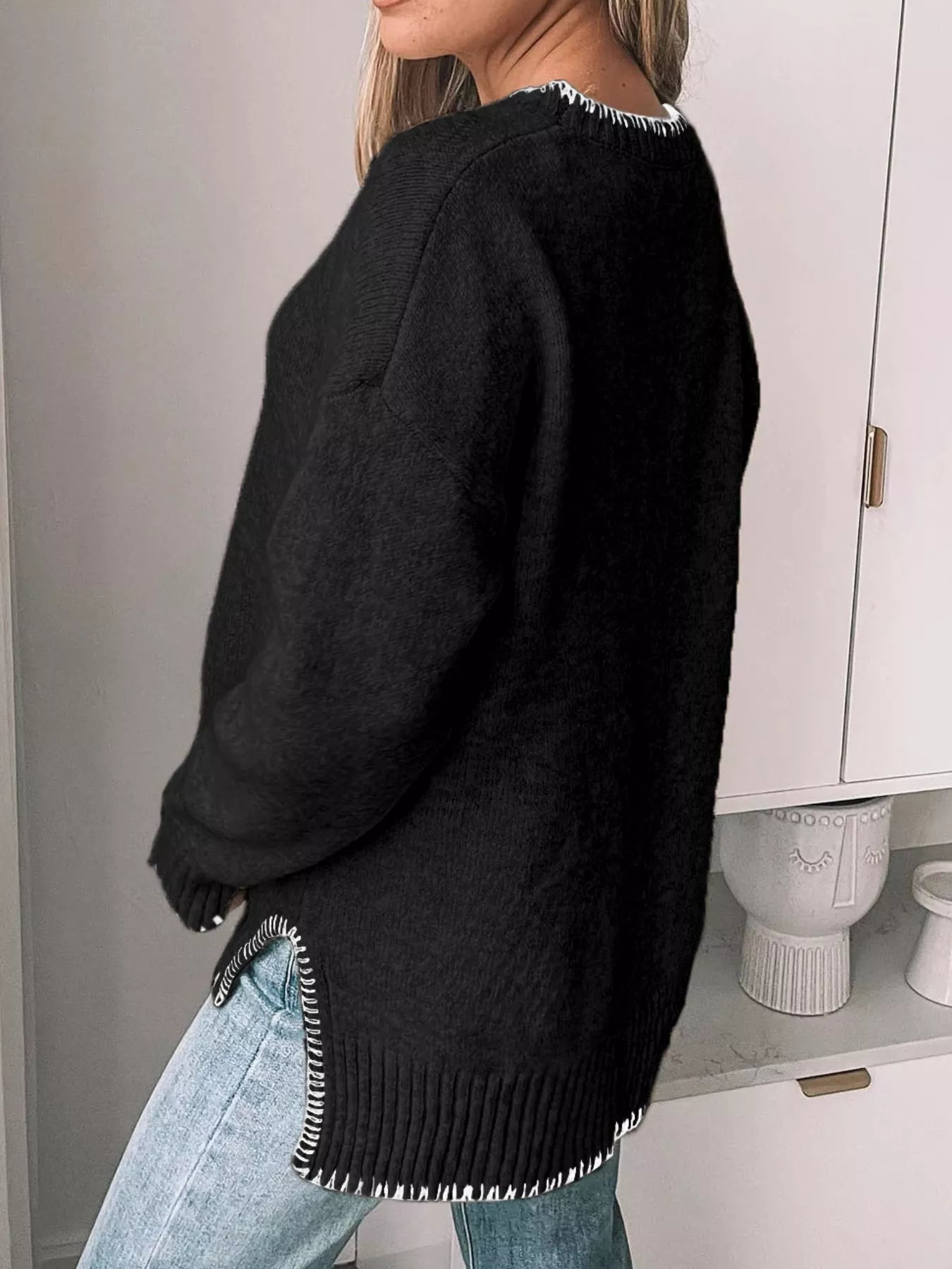 Person wearing a black sweater with fringe details in a minimal indoor setting.