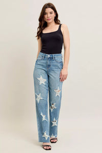 Woman wearing blue jeans with star patterns and a black top on a beige background