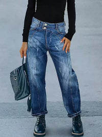Person wearing blue jeans and black boots holding a gray backpack against a plain background