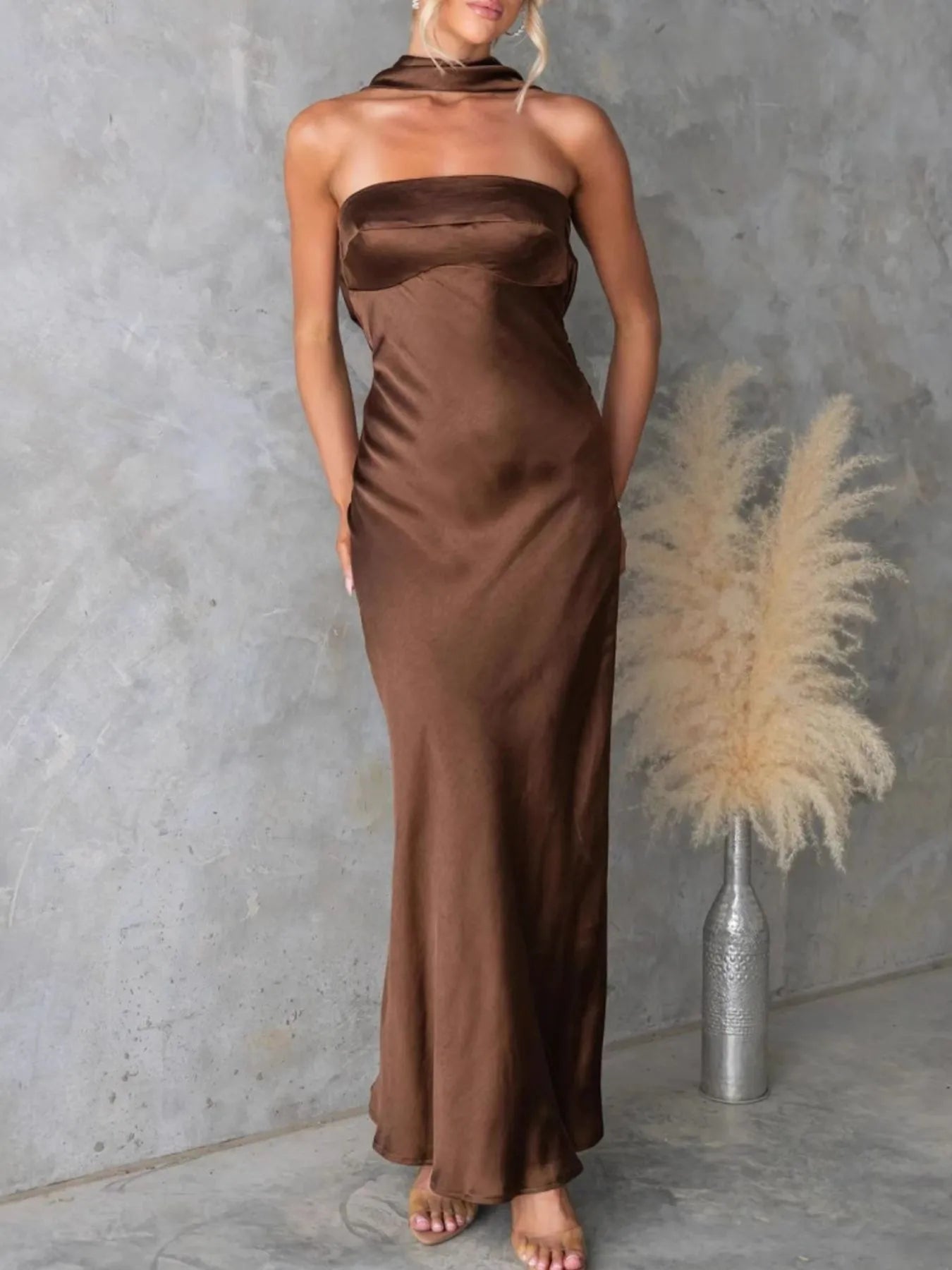 Woman wearing a brown satin halter neck dress against a gray wall with decorative elements.